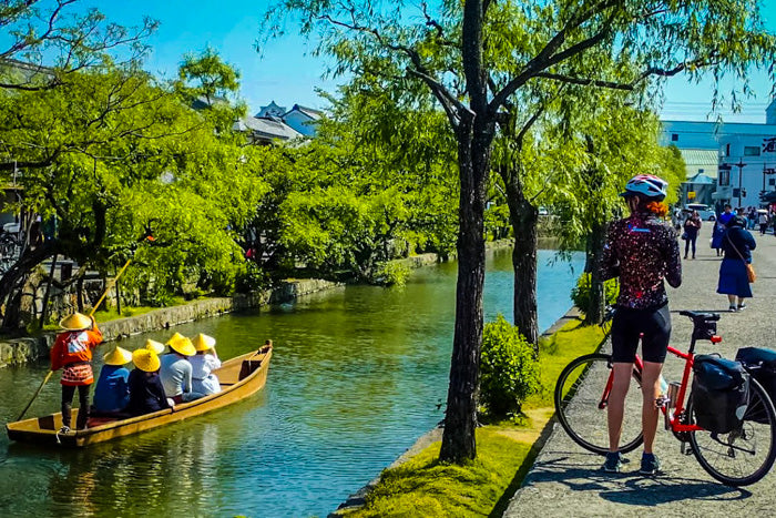 Un cycliste s'arrête le long d'un canal où l'on pousse un bateau à Kyoto.